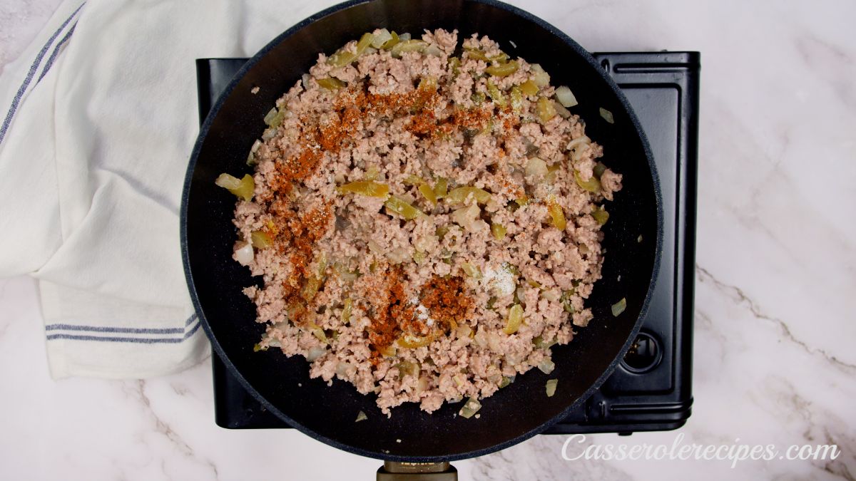 cooked ground meat being seasoned in skillet on black hot plate