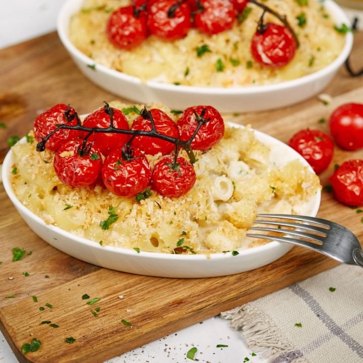two white ramekins of shrimp casserole topped by red tomatoes on cutting board