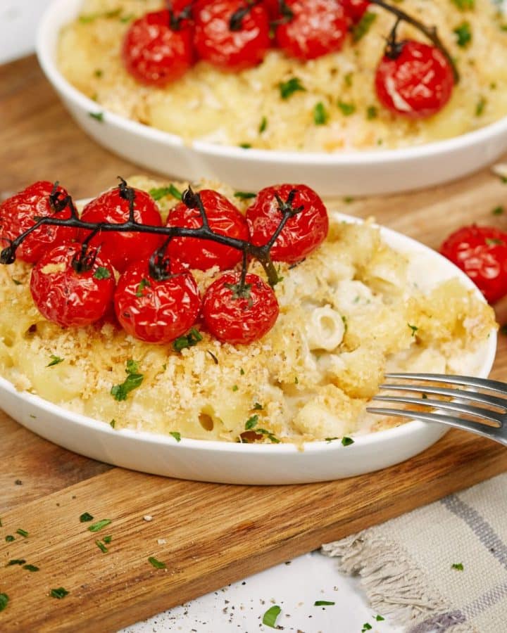 two white ramekins of shrimp casserole topped by red tomatoes on cutting board