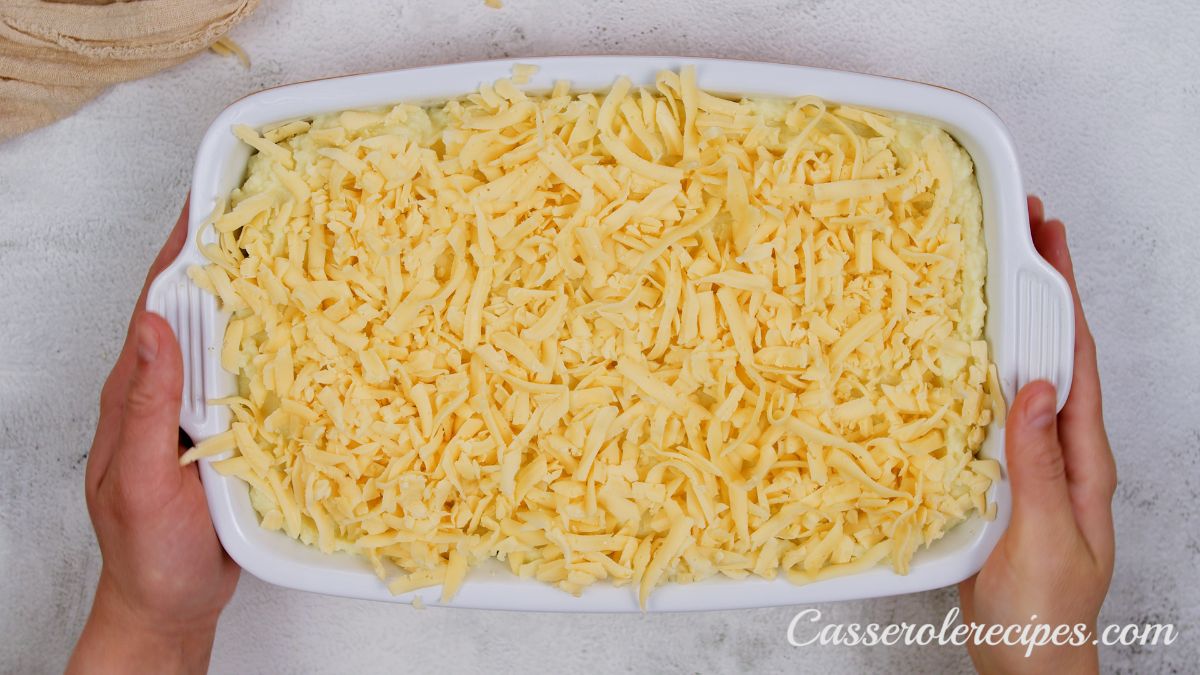 hands holding a white casserole dish topped with shredded cheese