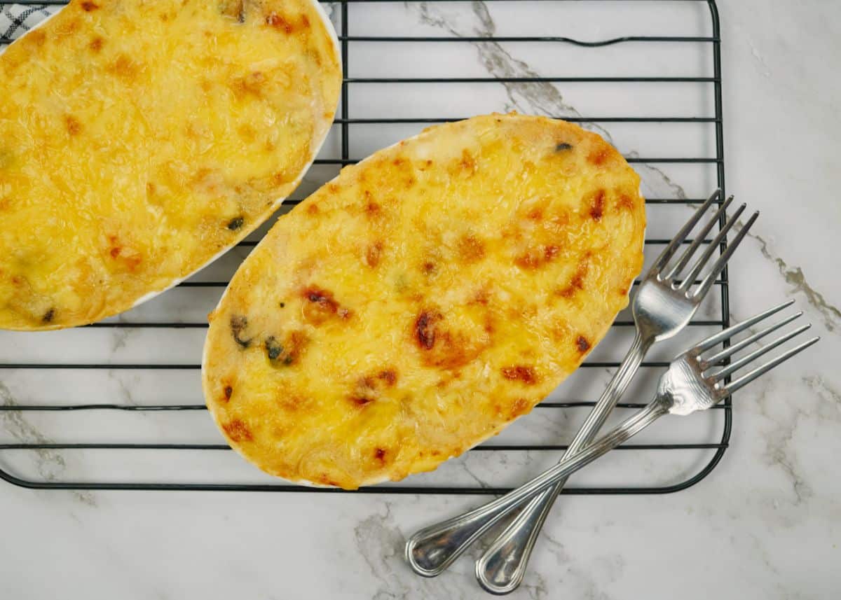 two ramekins of cheesy seafood casserole sitting on black wire rack over marble table