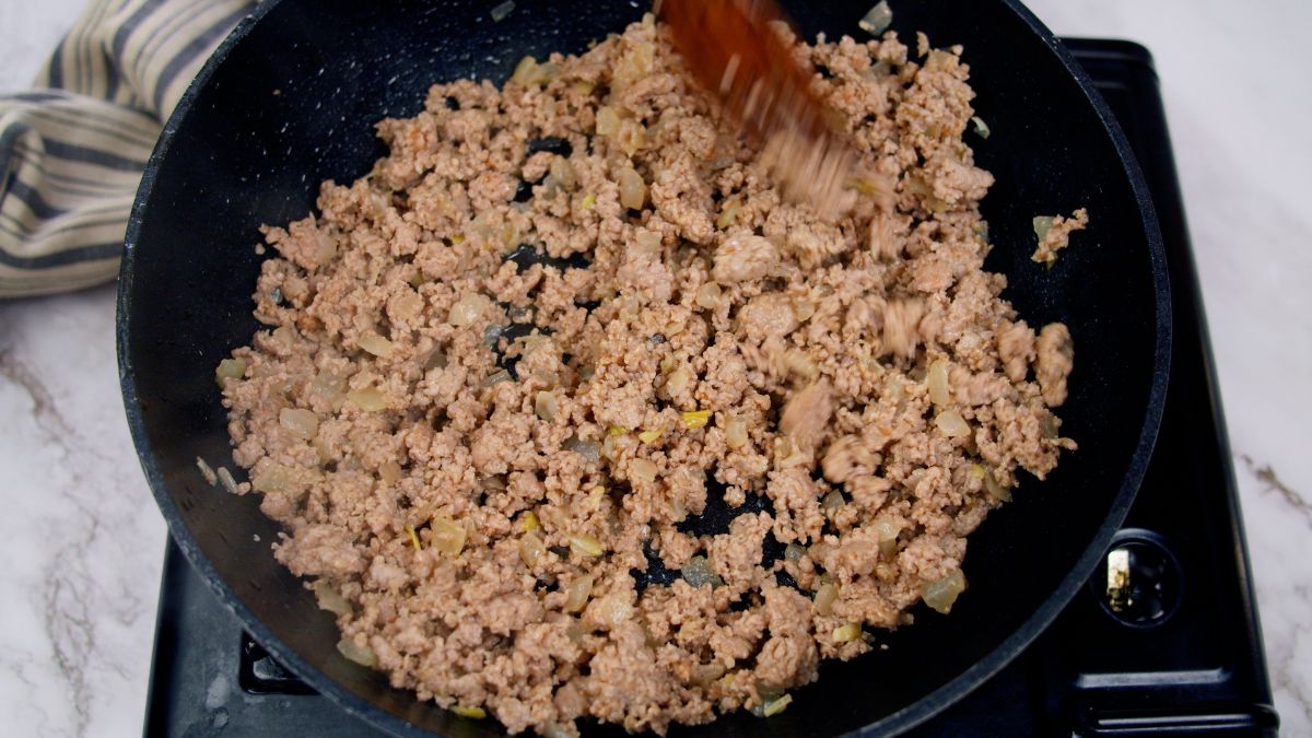 cooked ground meat in black skillet with wooden spoon