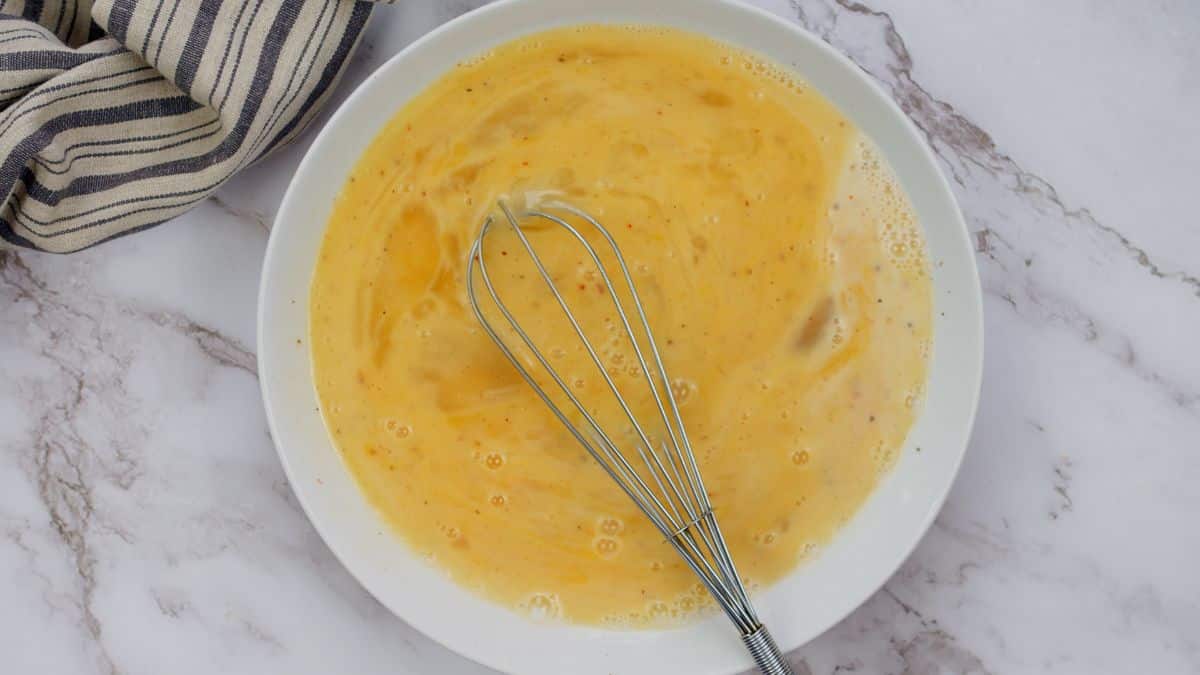white bowl of beaten eggs with whisk in bowl
