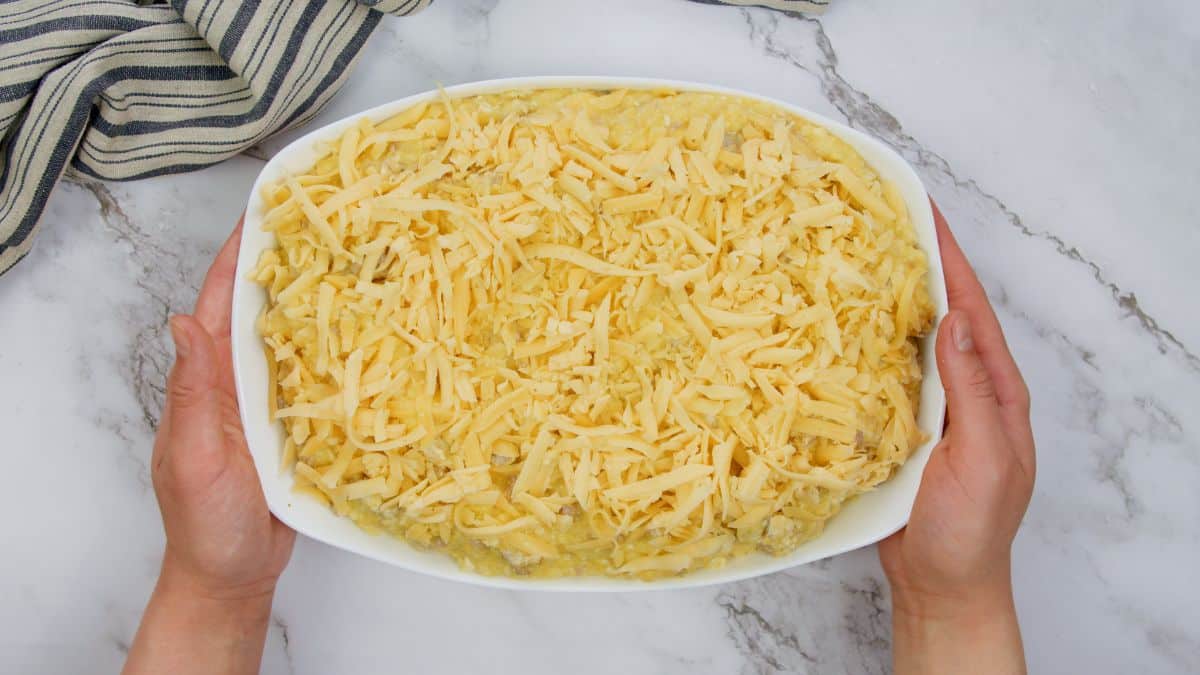 rectangle white casserole dish filled with ingredients with shredded cheese on top