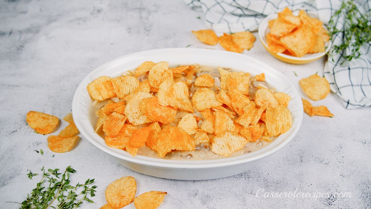 ridged potato chips being placed on top of tuna casserole in white baking dish