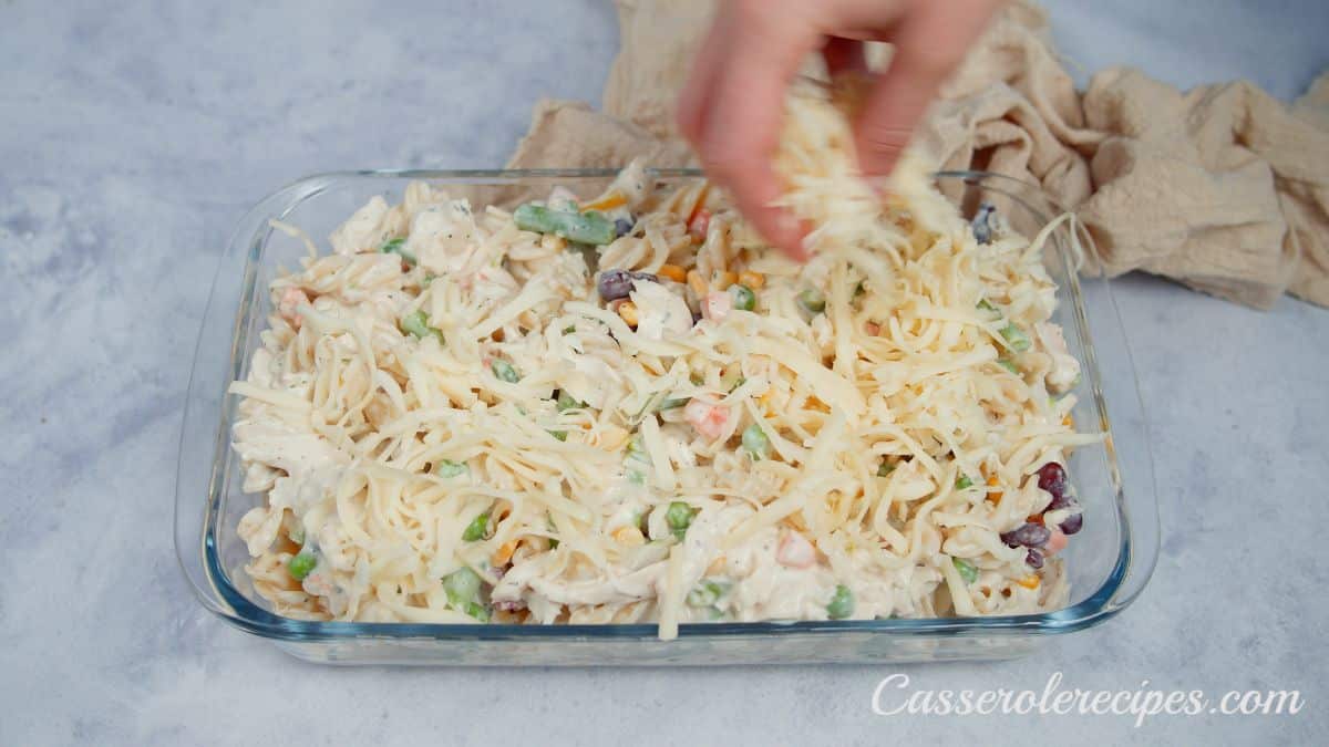 hand sprinkling cheese on top of uncooked casserole in glass dish