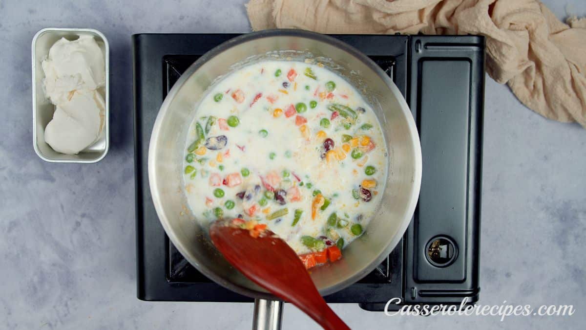 wooden spoon stirring vegetables and cream in skillet on hot plate