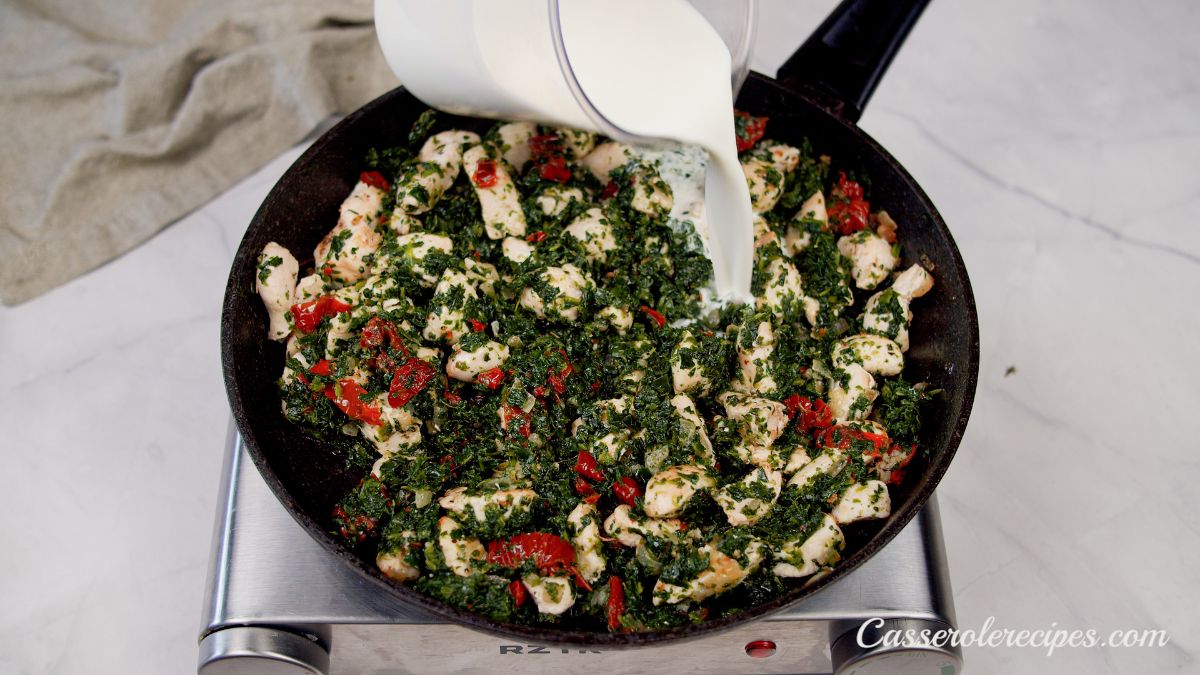 chicken and spinach in black skillet with milk being poured on top