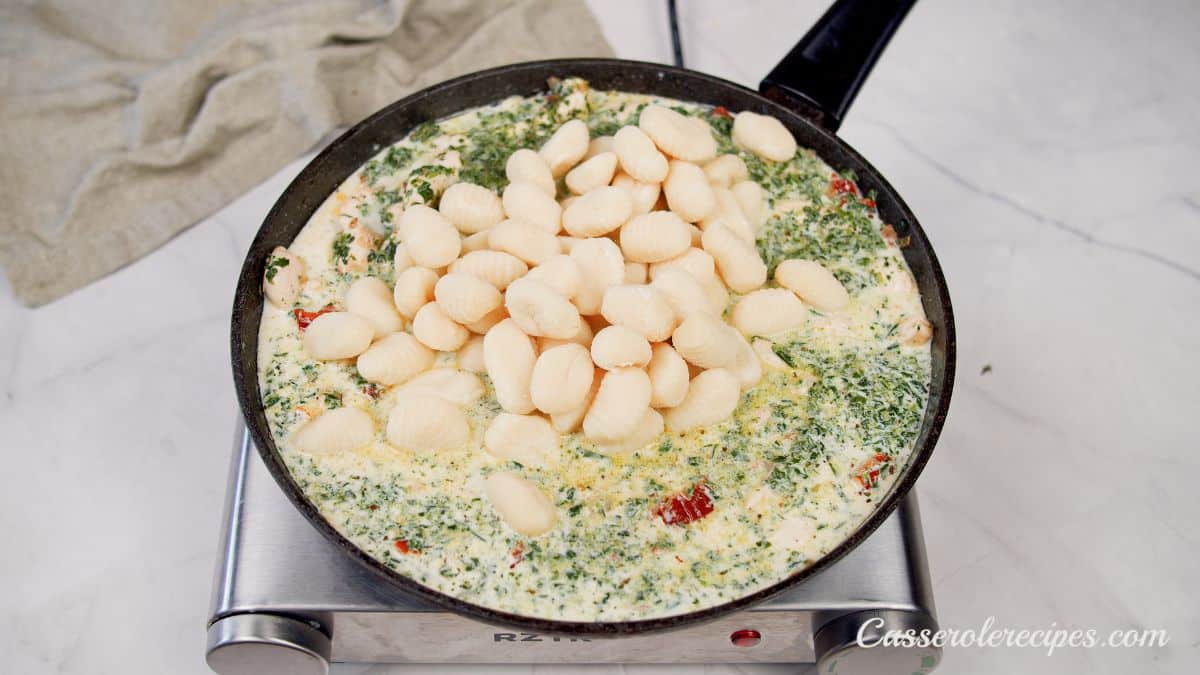 gnocchi being added to skillet of cream and spinach sauce