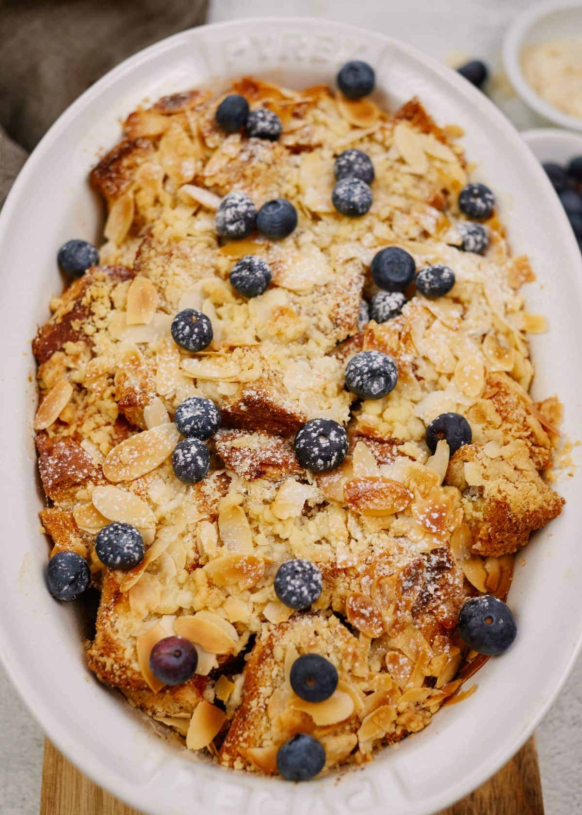 white oval baking dish of vegan french toast casserole topped with almond slivers and blueberries