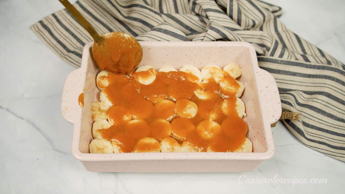 Spoon pouring caramel sauce over bananas in baking dish