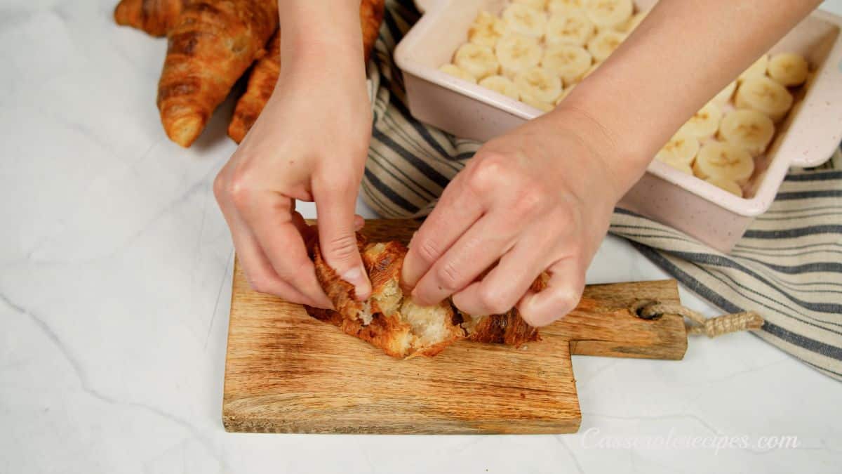 hand tearing apart croissant on cutting board