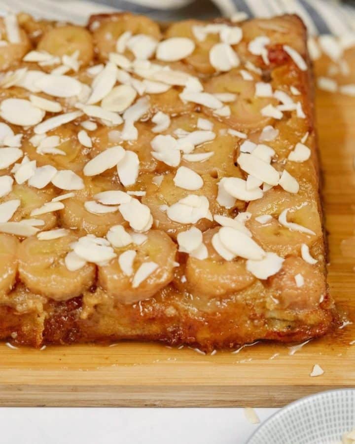 bananas foster breakfast casserole topped with almonds on top of wood cutting board