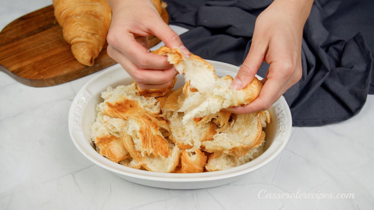 hands tearing apart croissants over baking dish