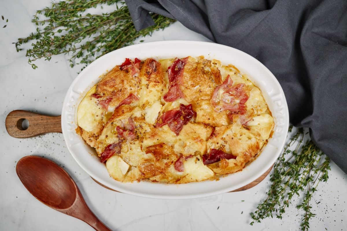 brie and proscuitto breakfast bake with croissants in white baking dish