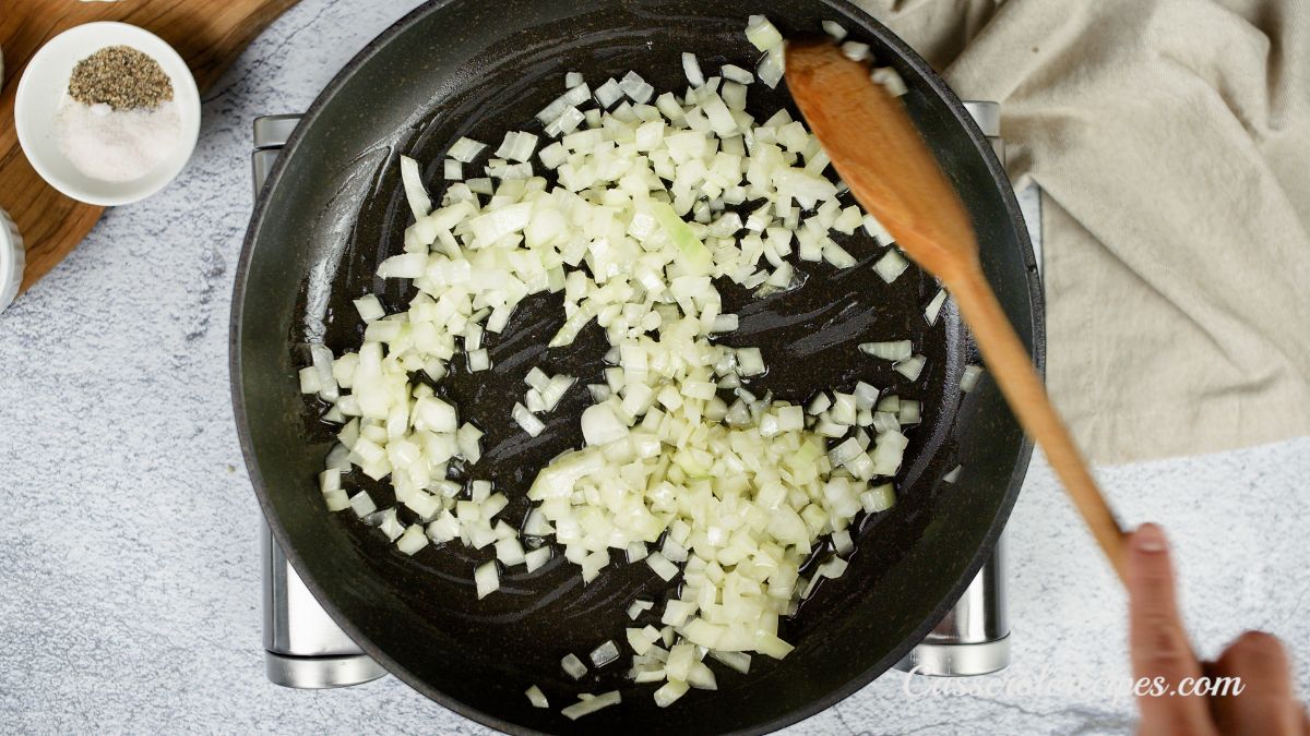wooden spoon stirring onions in black skillet on hot plate