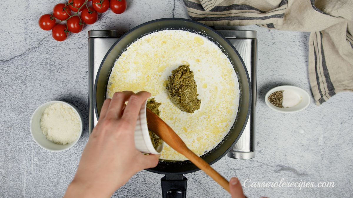 cream and pesto being stirred into sauce in skillet