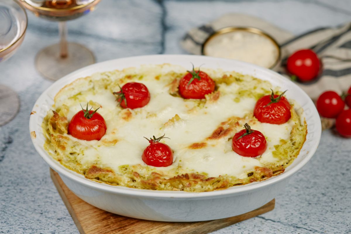 white oval baking dish of pasta cassserole topped by tomatoes and cheese