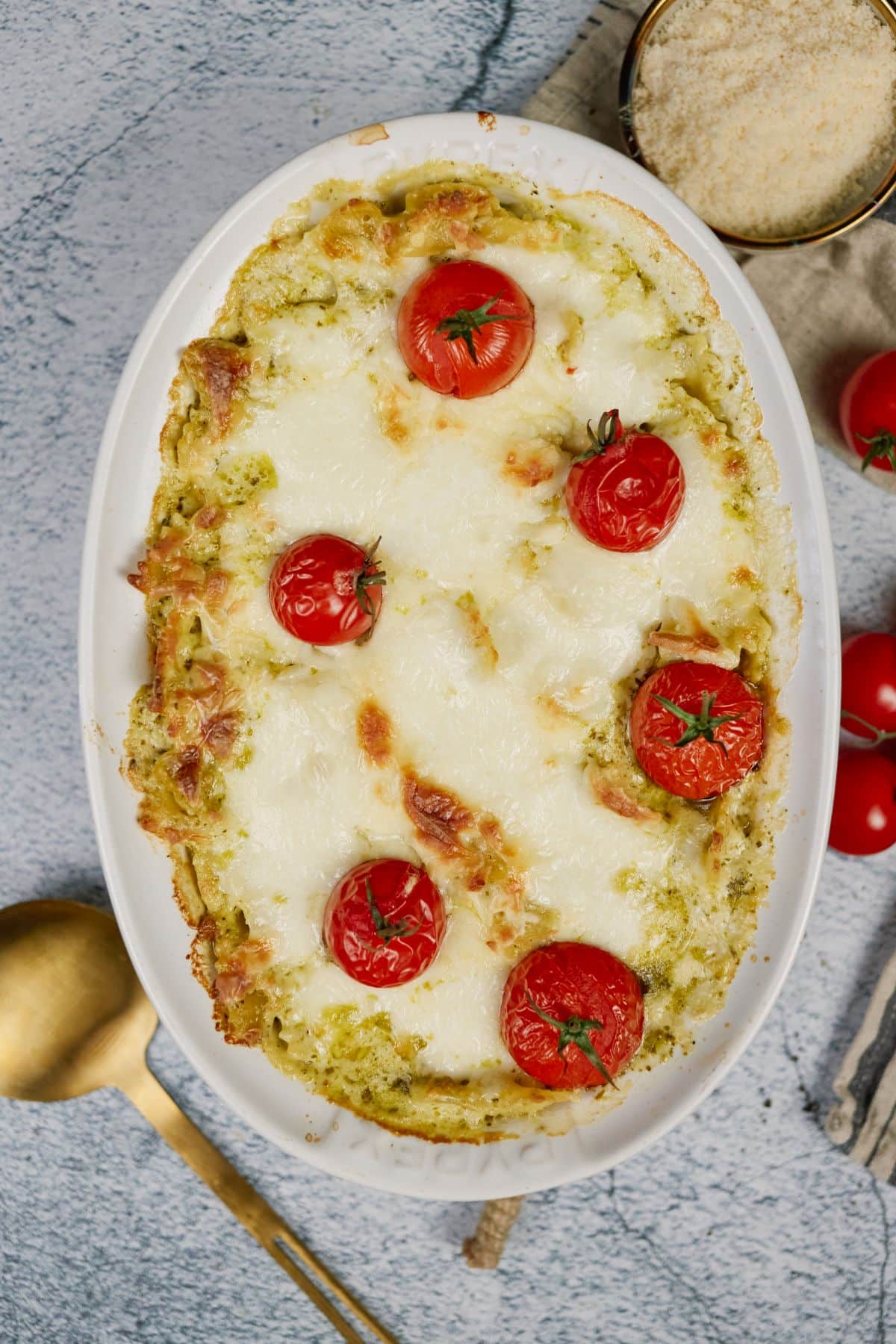 oval baking dish of pasta casserole topped by tomatoes on gray table