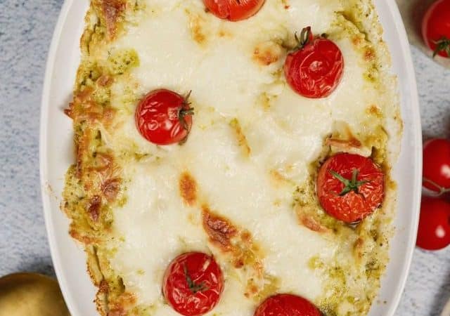 oval baking dish of pasta casserole topped by tomatoes on gray table