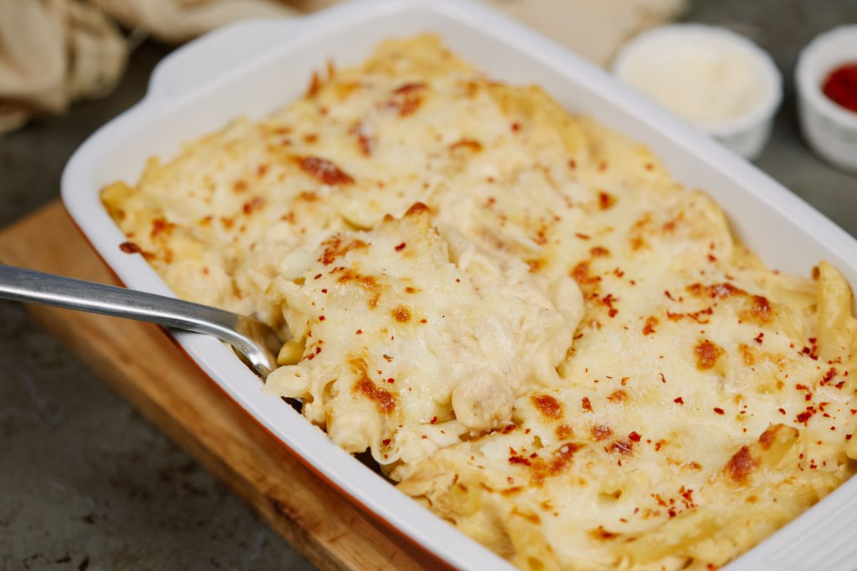 white and red baking dish of chicken cauliflower pasta with spoon in side of pan