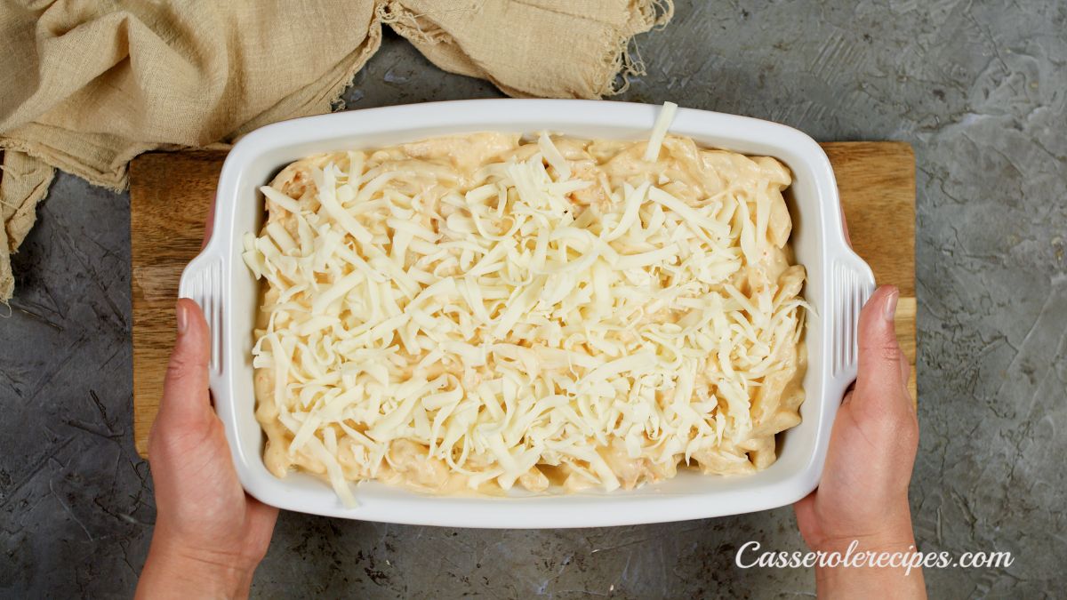 hands holding white baking dish of casserole covered with shredded cheese