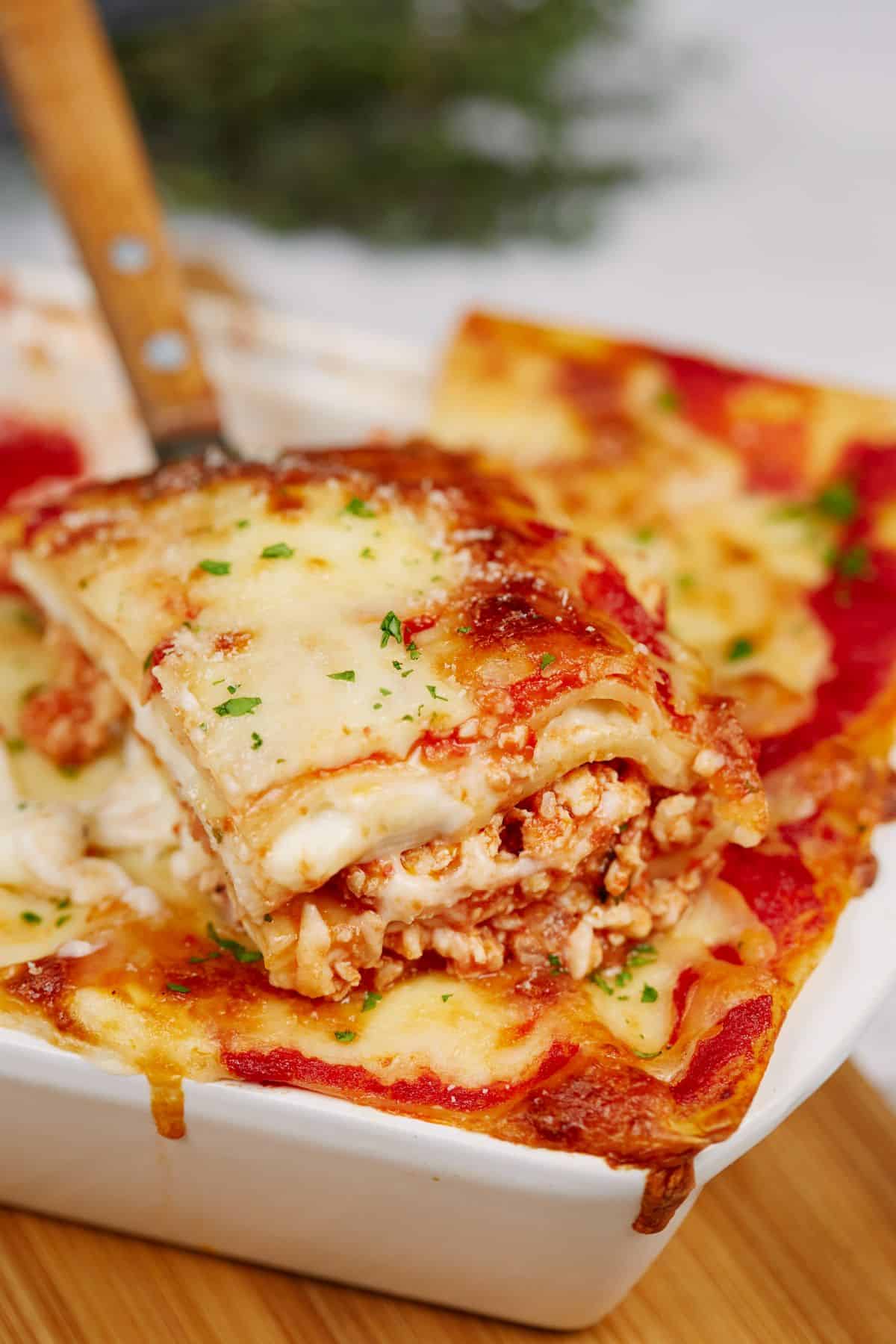 spatula holding a slice of chicken lasagna above baking dish