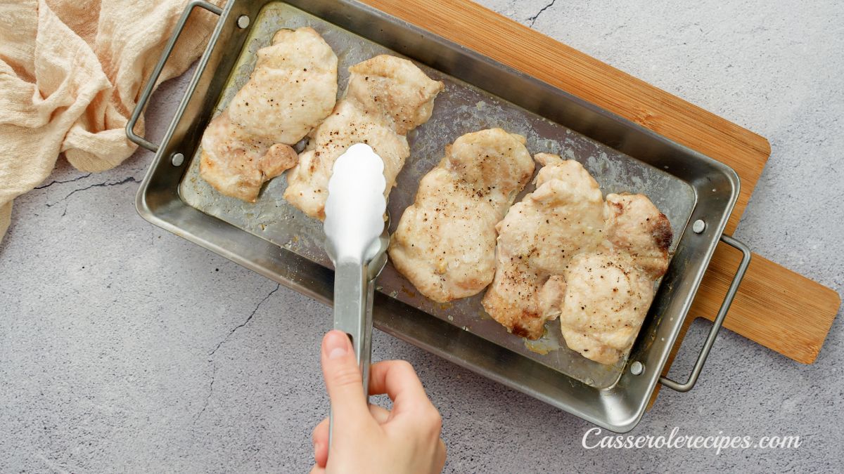 baking sheet of chicken thighs cooked with a white tong holding piece above pan