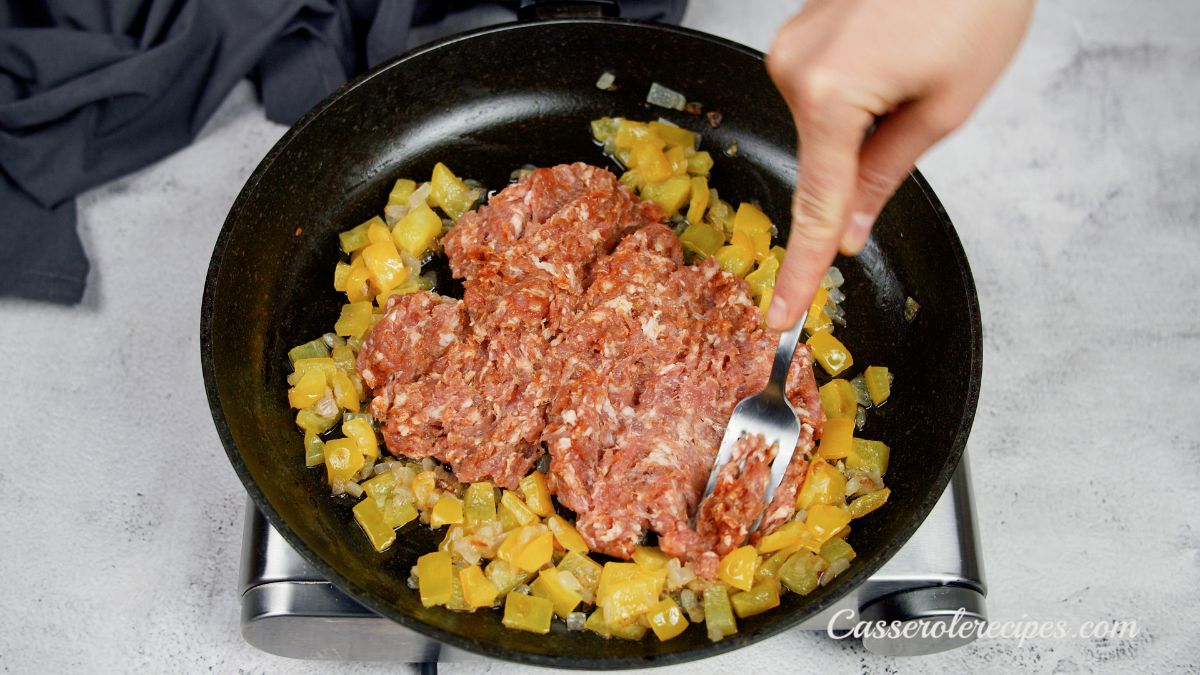 raw chorizo being added to skillet of onions