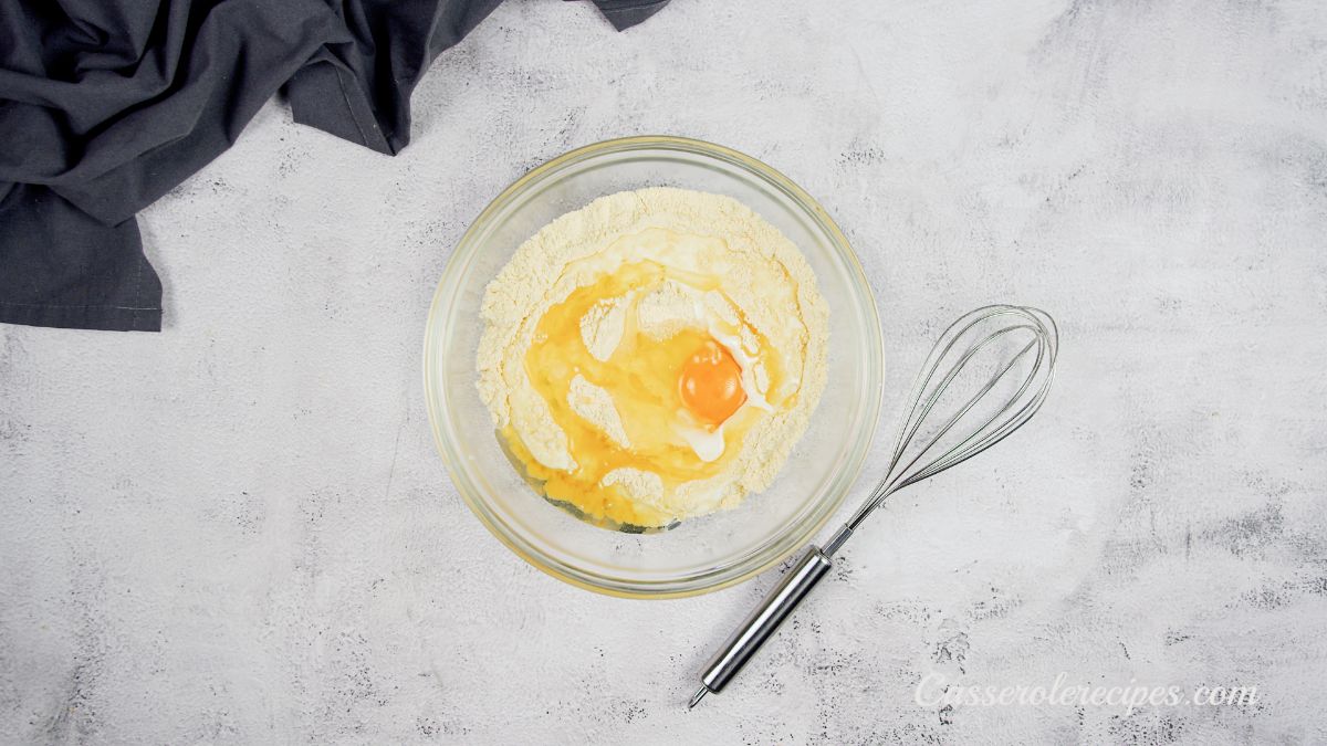 egg being stirred into cornbread batter in glass bowl