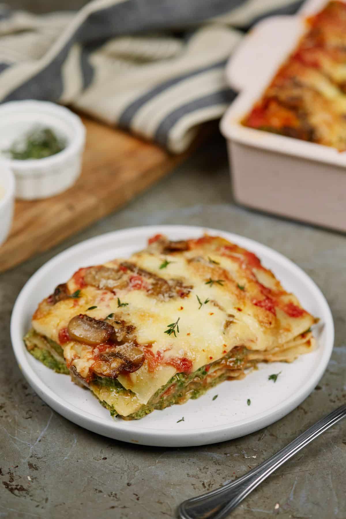 mushroom and spinach lasagna on white plate on counter by baking dish