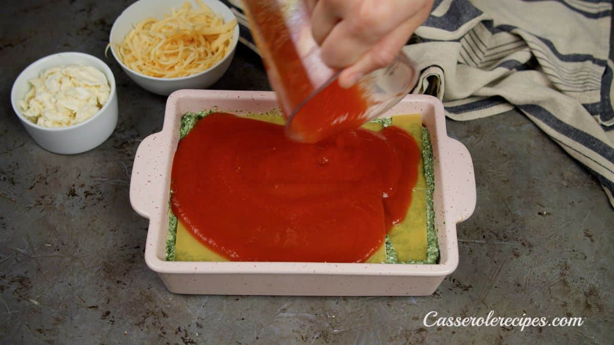 sauce being poured over noodles in baking dish