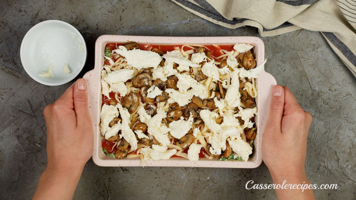 hands holding unbaked lasagna in pink baking dish