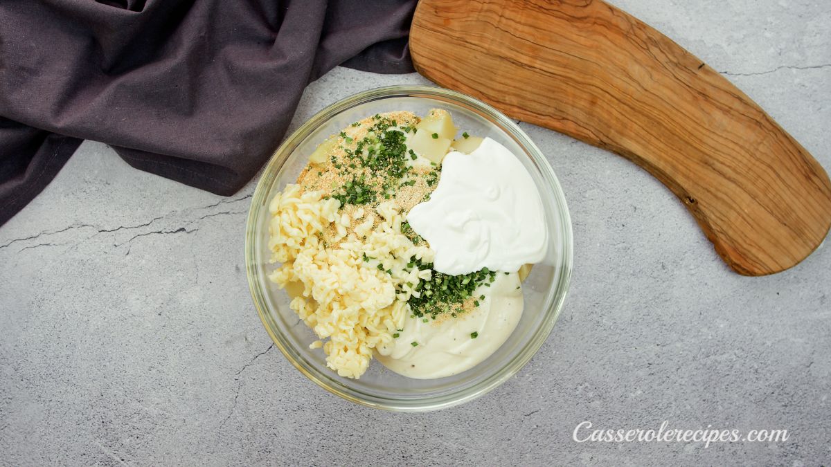 cheese and herbs in large glass bowl on counter by cutting board