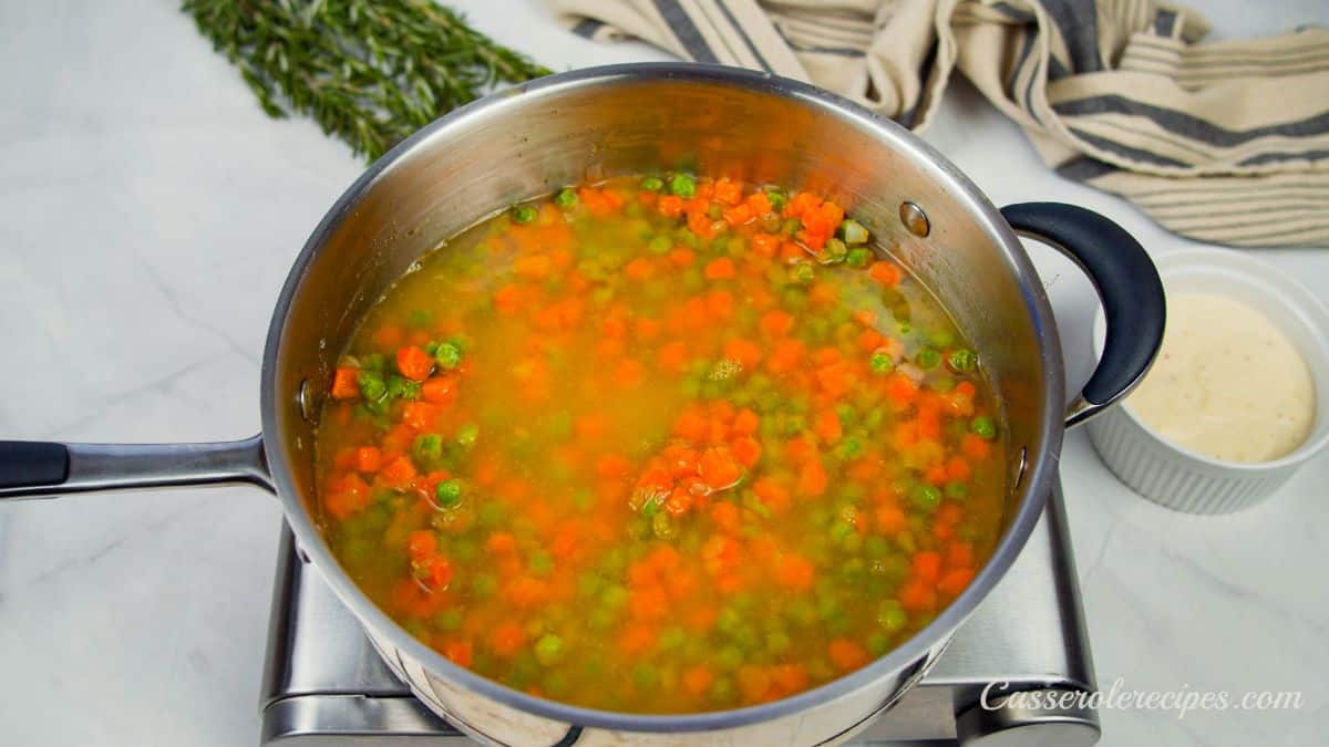 broth in skillet with cooked peas and carrots