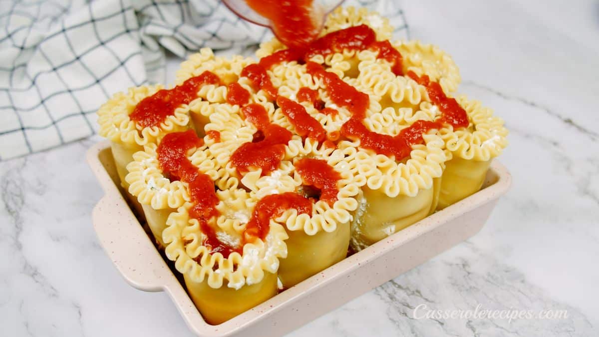 tomato sauce being spread on top of lasagna roll ups