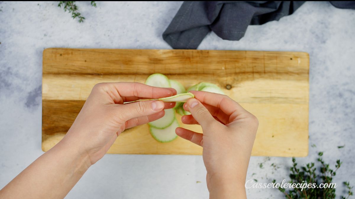 hand holding sliced zucchini above cutting board