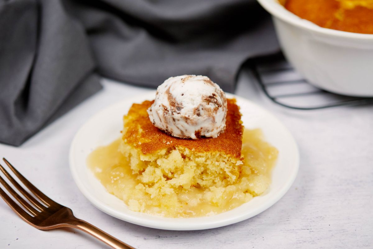 serving of butterscotch pudding casserole on round white dessert plate next to fork with gray napkin in background