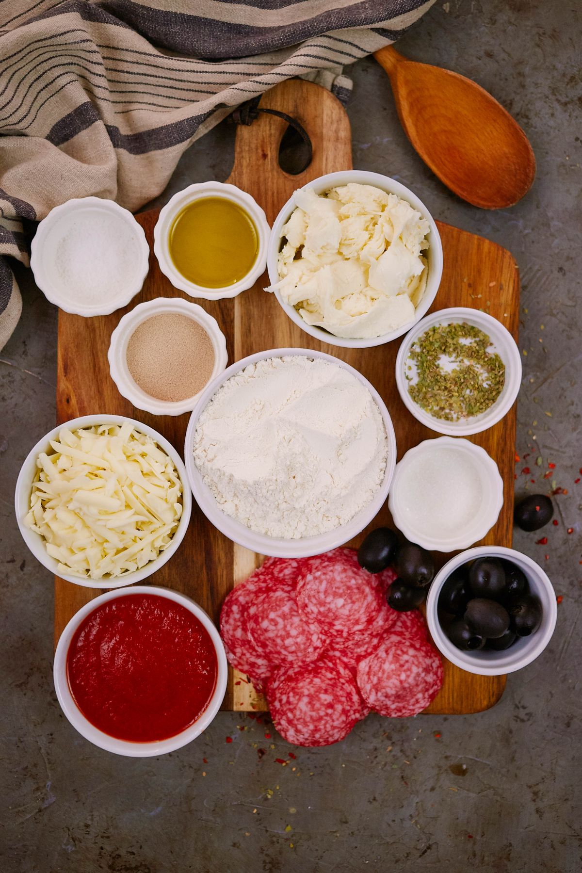 a variety of white ramkens filled with ingredients for making pizza sitting on wooden cutting board