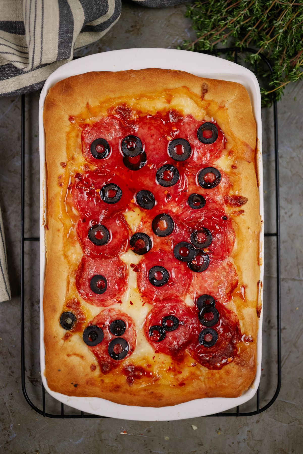 rectangular white casserole dish of cheesy deep dish pizza that is topped by sliced olives and pepperoni