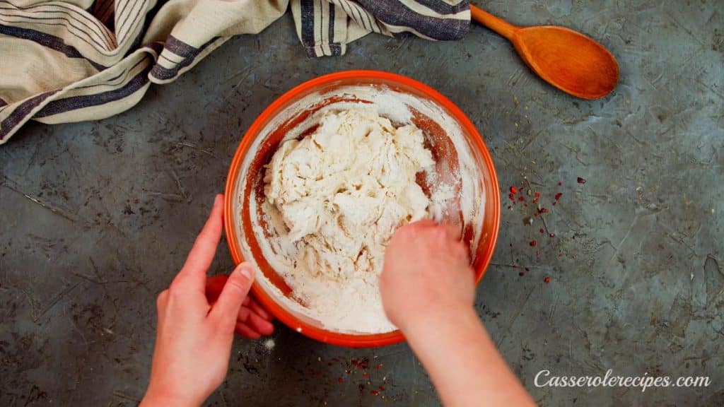 hand kneading pizza dough in large bowl