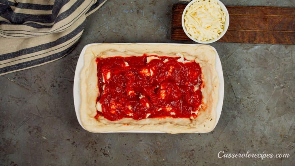 tomato sauce on top of cheese in baking dish on pizza crust