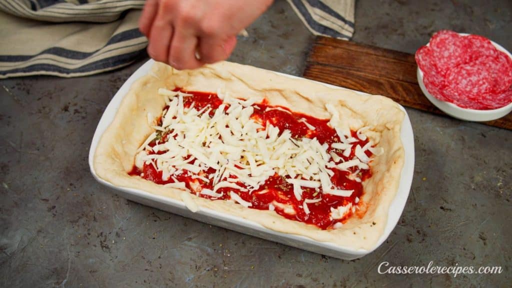 cheese being added to top of pizza in baking dish