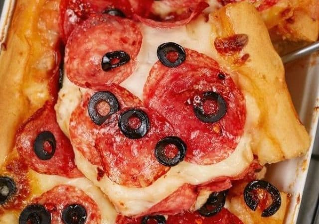 deep dish pizza topped with salami and olives in baking dish