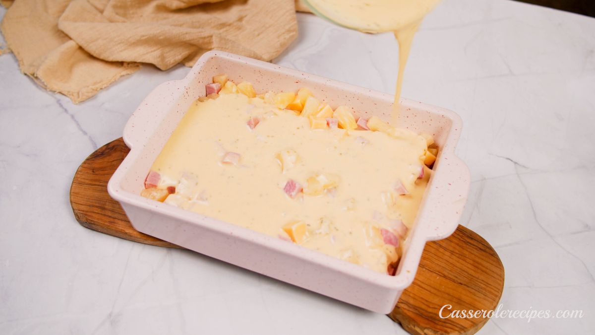 batter covering ham and pineapple in white baking dish