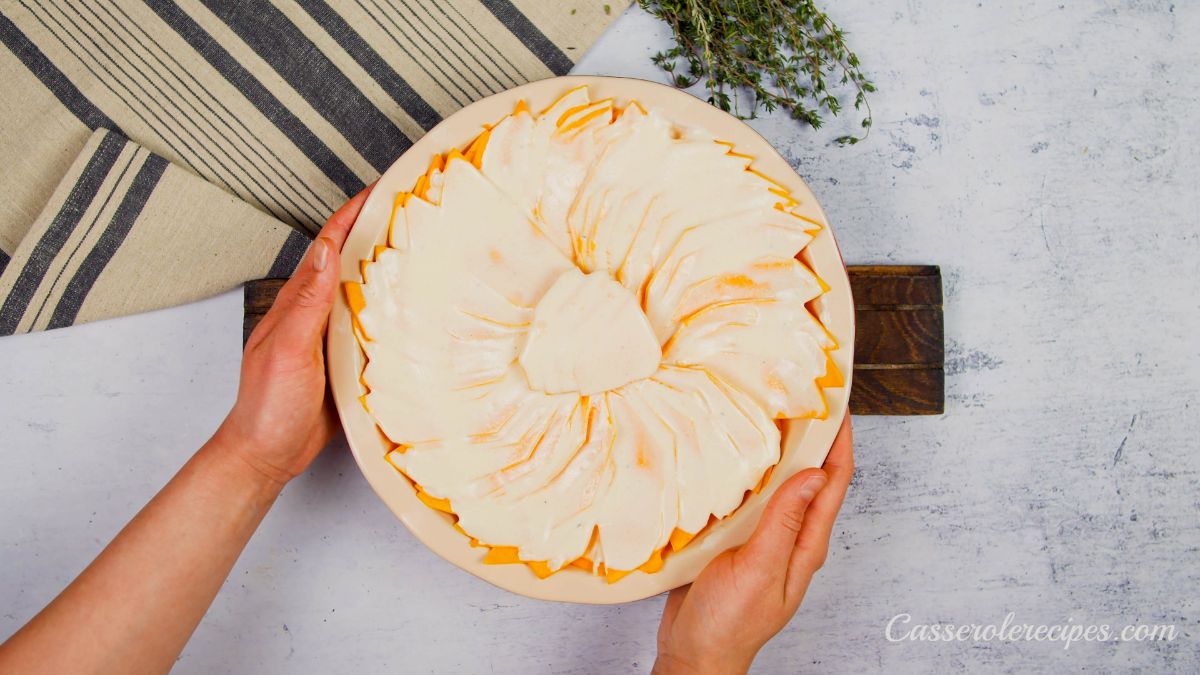 pumpkin gratin in round baking dish held above table with striped napkin