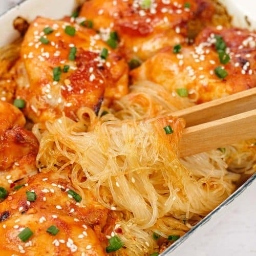 chopsticks lifting a bite of korean spicy chicken rice noodle bake from a casserole dish