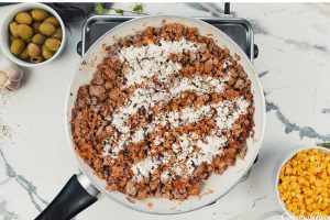 adding flour and other ingredients to a pan to make pastel de chocolo corn and beef casserole