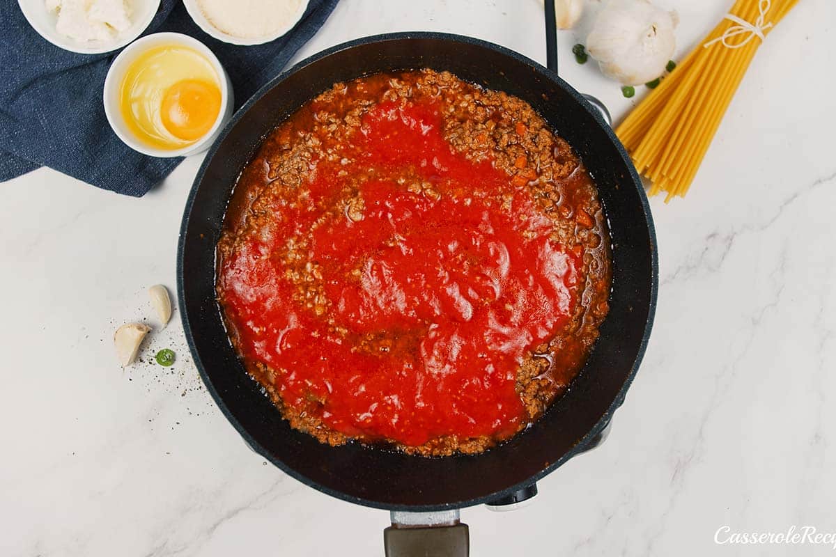 tomato sauce being added to the other ingredients to make pastitsio greek beef pasta bake