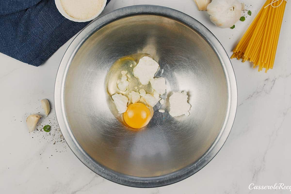 egg and other ingredients being combined to make pastitsio greek beef pasta bake